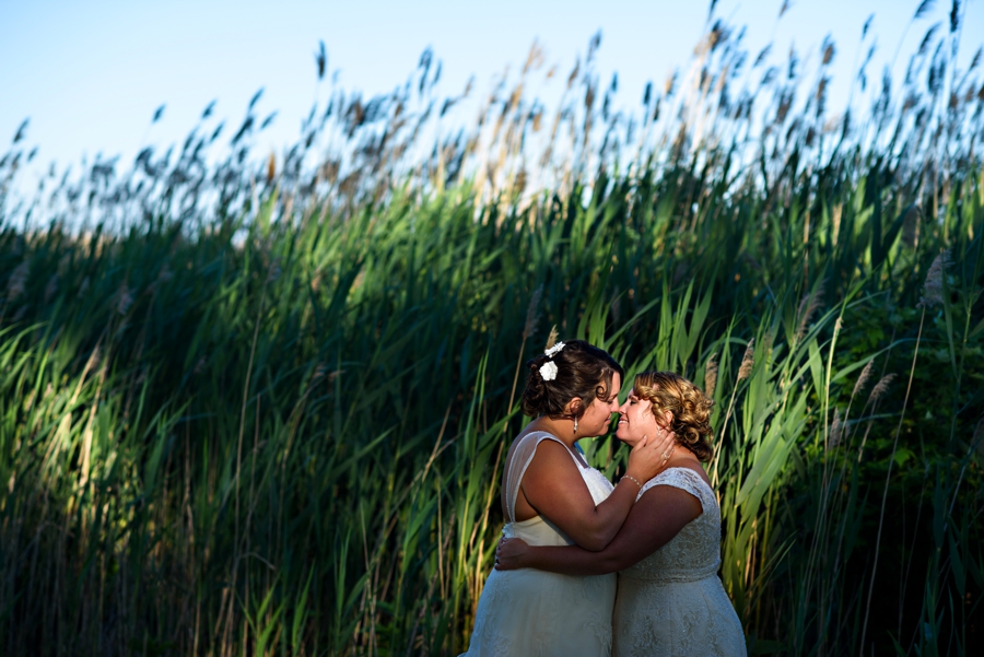 A bride bringing her wife in for a kiss in the setting sunlight.